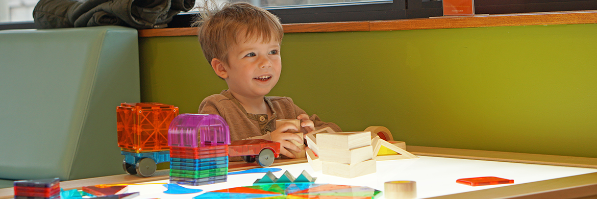 Toddler boy playing with colorful blocks in the youth services area of the library